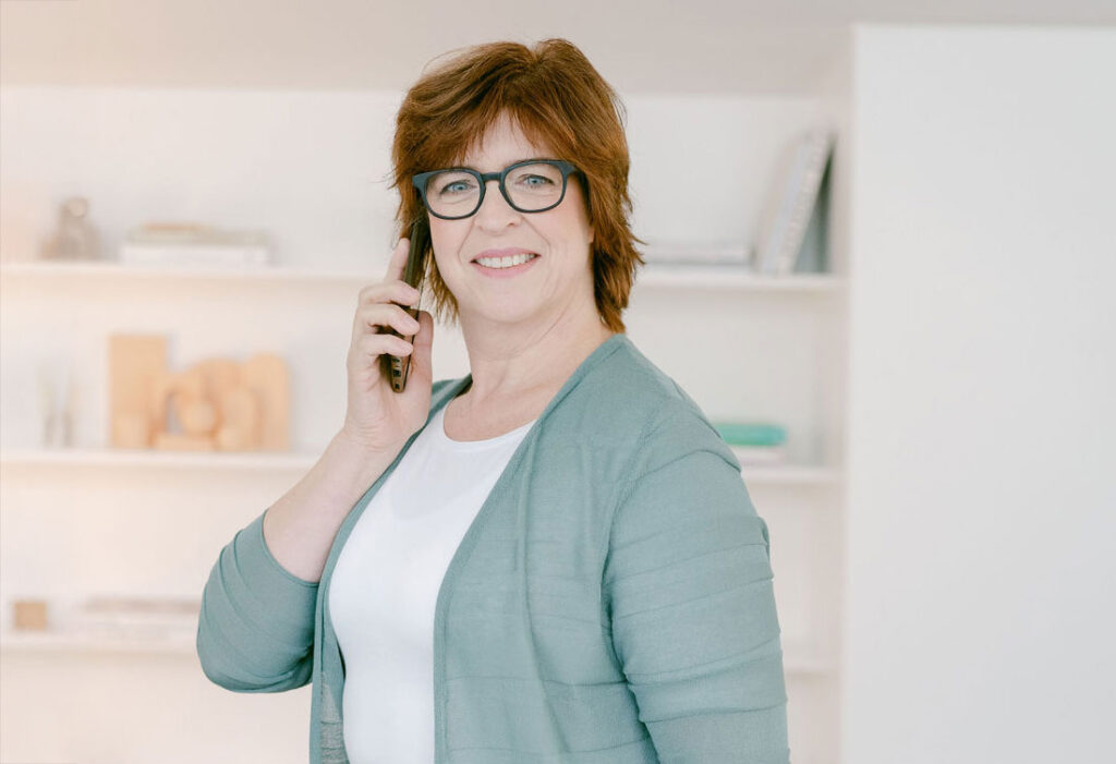 Veronika von Rüden steht in ihrem Büro und telefoniert mit ihrem Handy, lächelt und blickt direkt in die Kamera